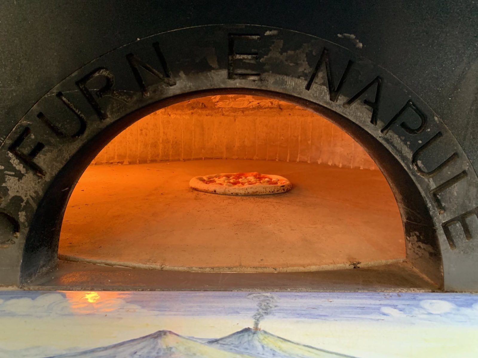 Nápolyi fatüzelésű kemence izzó boltíves szája, benne sülő pizza