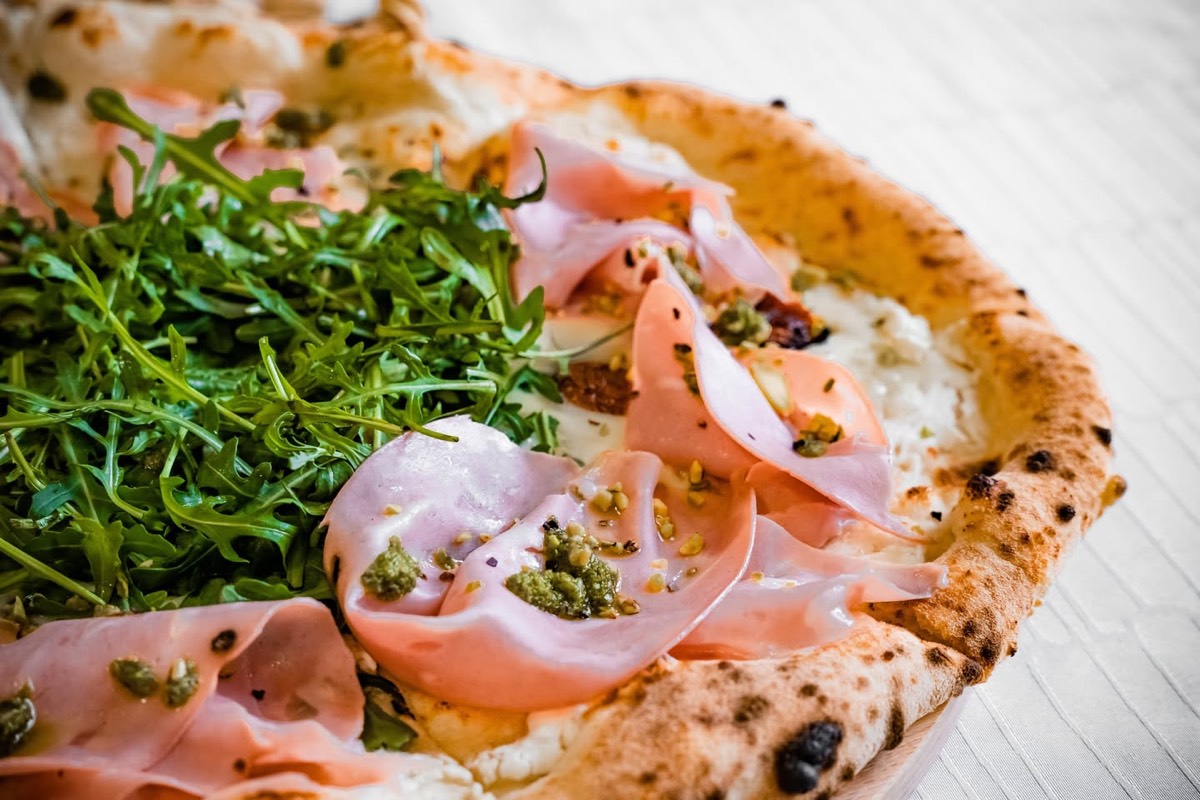 Fehér alapú pizza rukkolával, mortadellával és pisztáciás pestóval, közelről