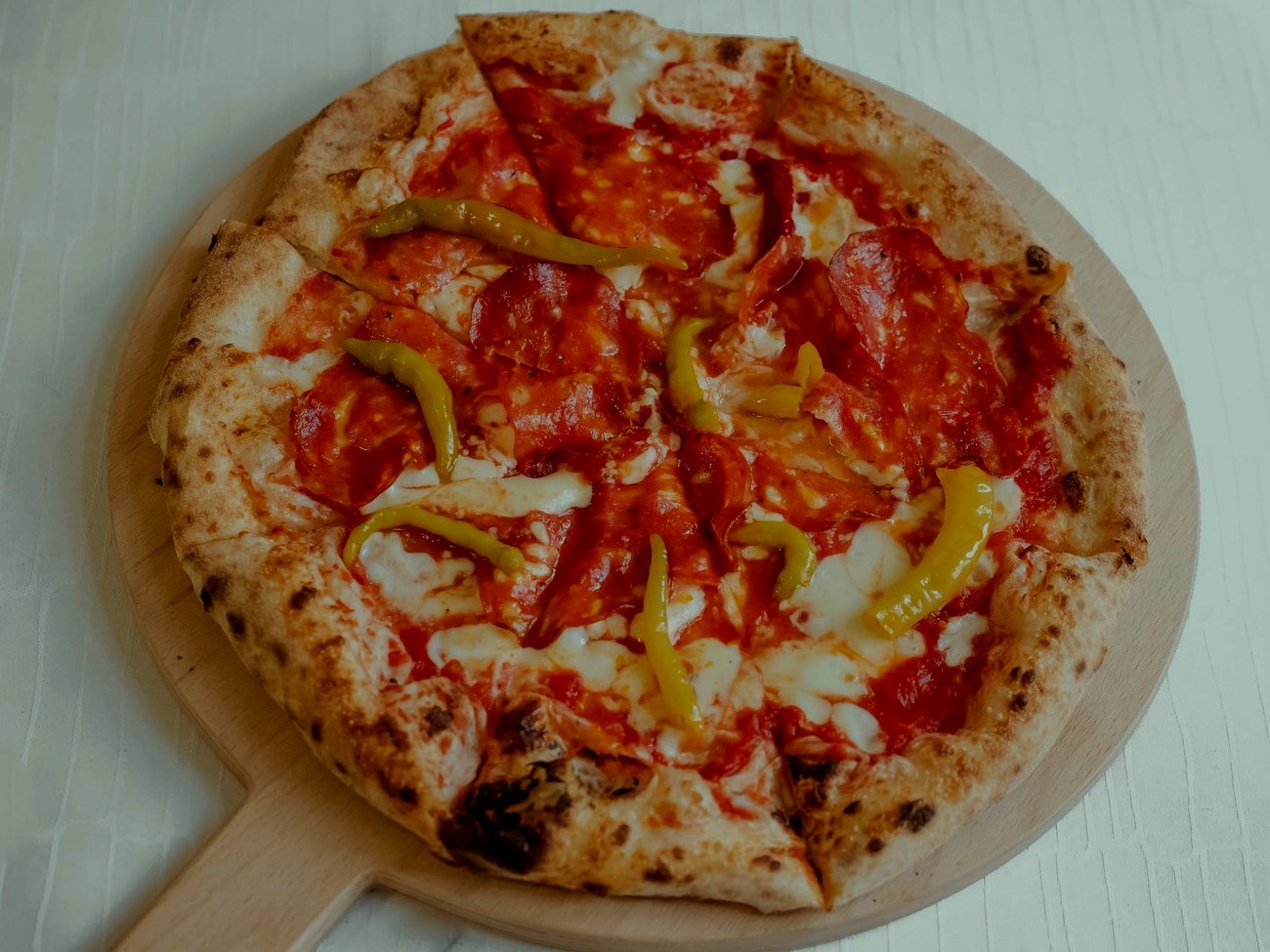 Egész, paradicsomos pizza fatálcán, hegyes erős paprika csíkokkal megrakva